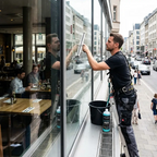 Profi-Glasreiniger mit MILURY Glasreiniger auf einer Leiter und wischt ein Fenster ab.